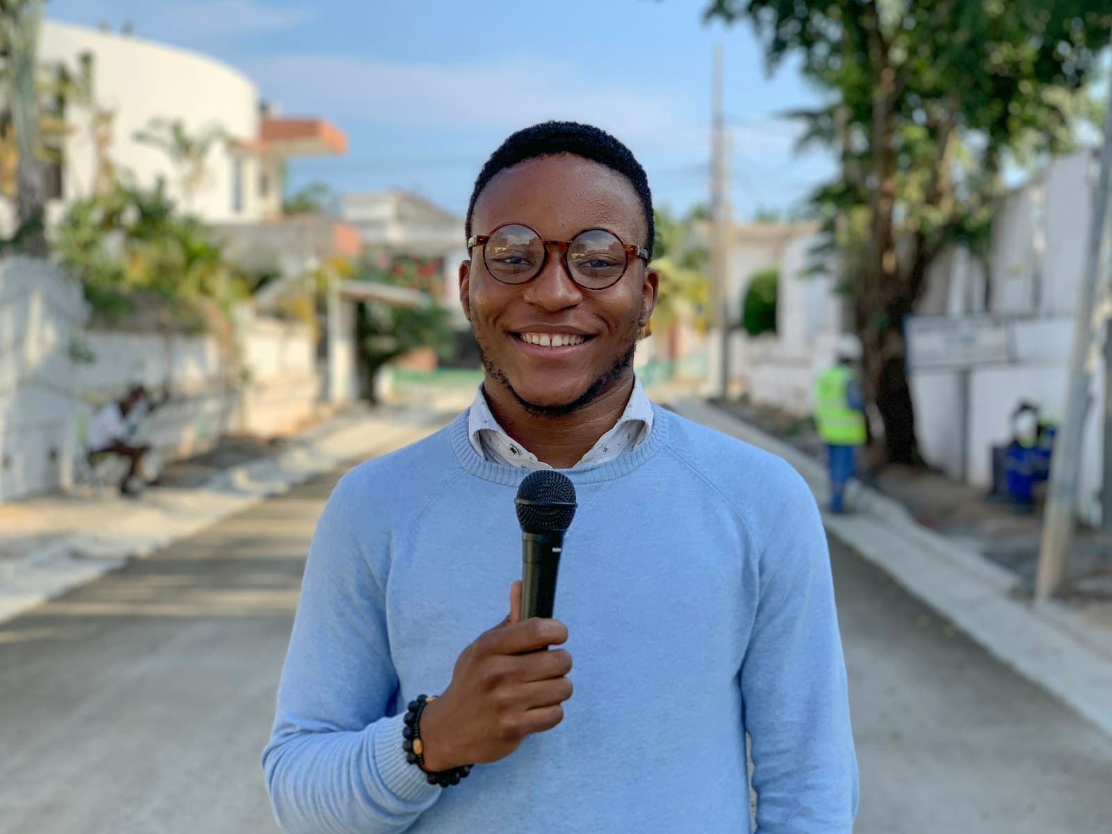 A young reporter holds a microphone on a neighborhood street.
