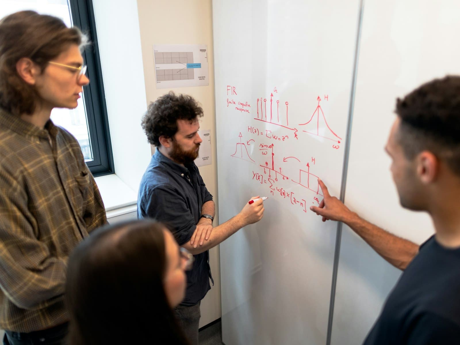 Four people work through a complex diagram together at a whiteboard.